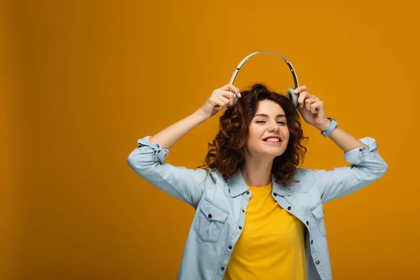 Щаслива руда дівчина посміхається, тримаючи навушники на помаранчевому — стокове фото