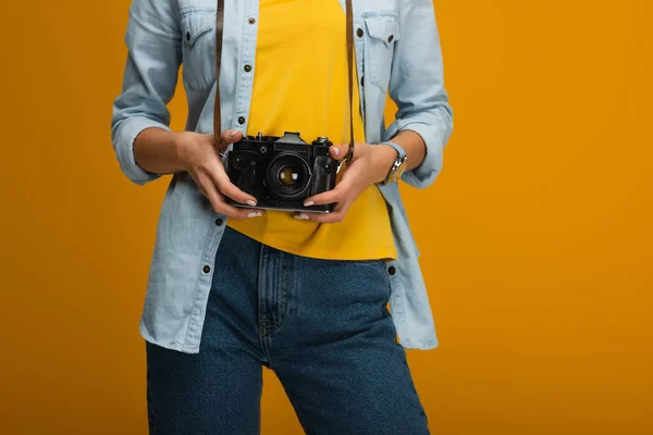 Обрезанный вид молодой женщины, стоящей и держащей цифровую камеру на оранжевом — стоковое фото