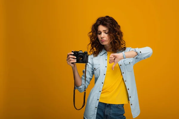 Sconvolto fotografo rossa tenendo la fotocamera digitale e mostrando pollice verso il basso su arancione — Foto stock