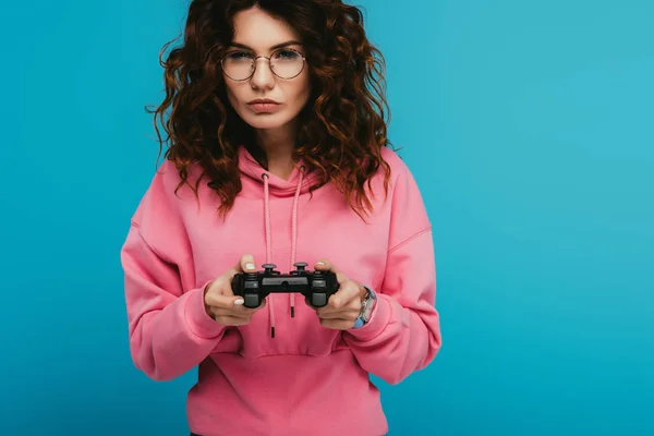 Serious curly redhead girl playing video game while holding joystick on blue — Stock Photo