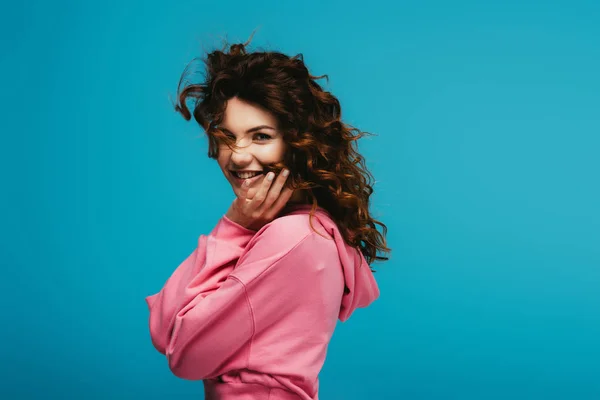 Cheerful pretty girl with curly red hair looking at camera on blue — Stock Photo