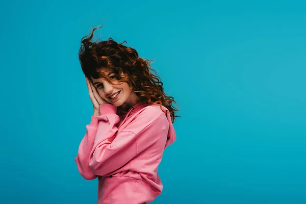 Heureuse jeune femme aux cheveux roux bouclés regardant la caméra sur bleu — Photo de stock