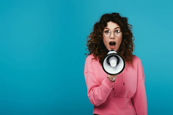 Menina ruiva atraente gritando enquanto segurando megafone em azul — Fotografia de Stock