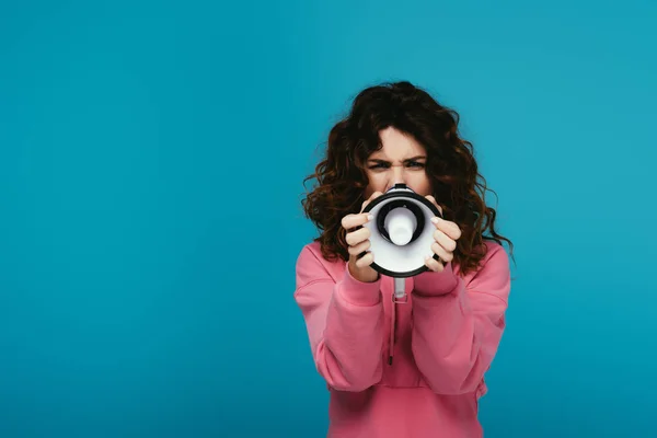 Curly redhead girl covering face with megaphone while screaming on blue — Stock Photo