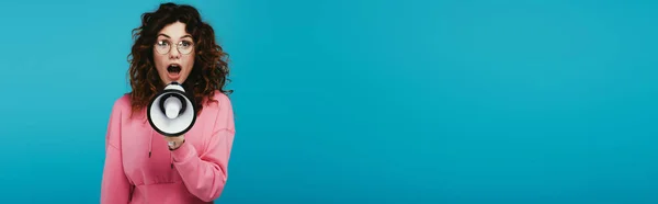 Panoramaaufnahme eines attraktiven rothaarigen Mädchens, das schreit, während es ein Megafon auf blauem Grund hält — Stockfoto