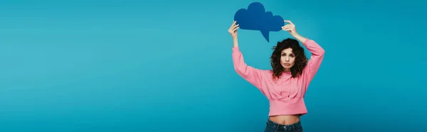 Panoramic shot of upset curly redhead girl holding thought bubble on blue — Stock Photo