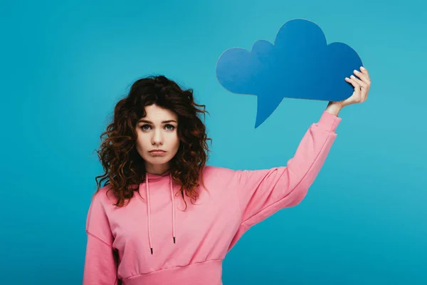 Upset curly redhead girl holding thought bubble on blue — Stock Photo