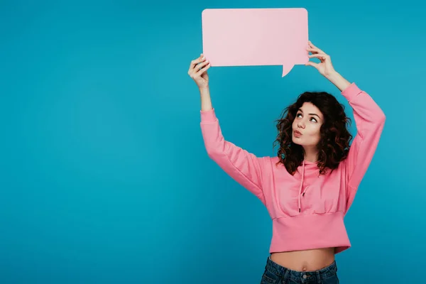 Attraente ragazza riccia con anatra faccia tenendo rosa discorso bolla su blu — Foto stock