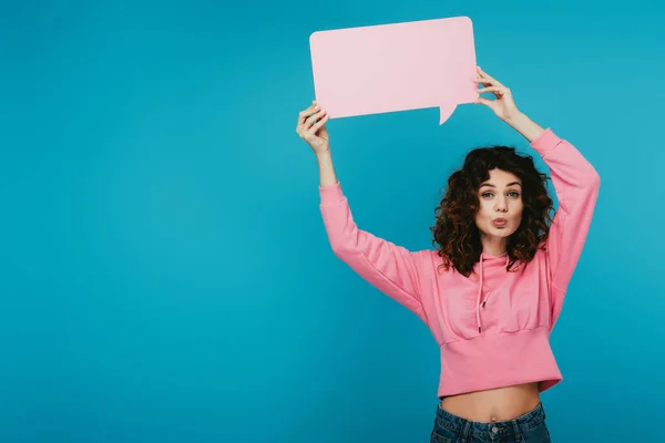 Curly redhead woman with duck face holding pink speech bubble on blue — Stock Photo