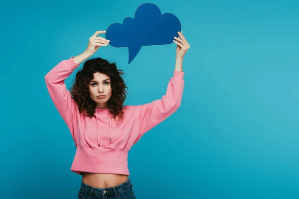 Sad curly redhead girl holding thought bubble on blue — Stock Photo