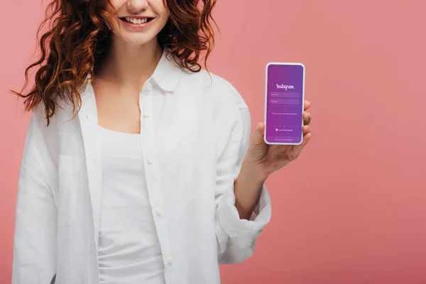 Cropped view of cheerful girl holding smartphone with instagram app on screen on pink — Stock Photo