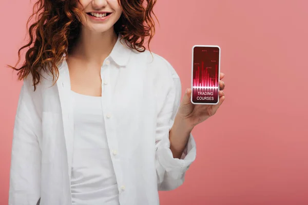 Cropped view of cheerful girl holding smartphone with trading courses on screen on pink — Stock Photo