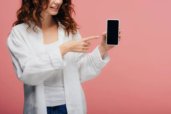 Ausgeschnittene Ansicht eines fröhlichen Mädchens, das mit dem Finger auf ein Smartphone mit leerem Bildschirm auf rosa zeigt — Stockfoto