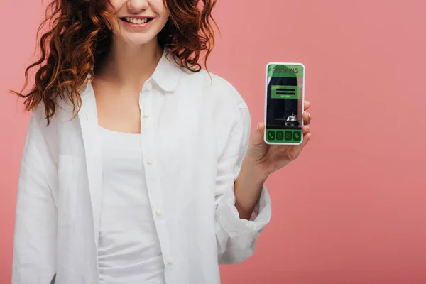 Ausgeschnittene Ansicht eines fröhlichen Mädchens mit Smartphone und Buchungs-App auf dem Bildschirm auf rosa — Stockfoto