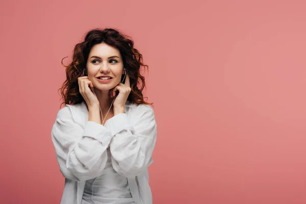 Happy curly girl listening music in earphones while standing on pink — Stock Photo