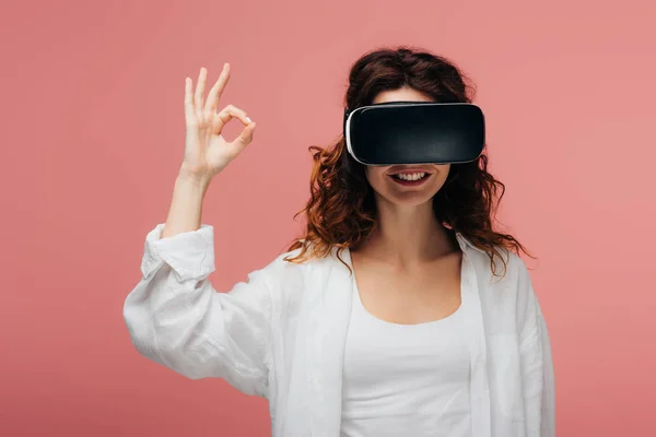 Glücklich lockige rothaarige Frau trägt Virtual-Reality-Headset und zeigt ok Zeichen auf rosa — Stockfoto