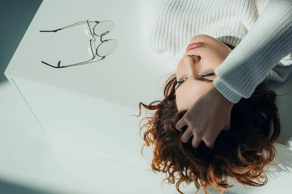 Vue aérienne de jolie rousse bouclée fille couché près de lunettes sur blanc — Photo de stock