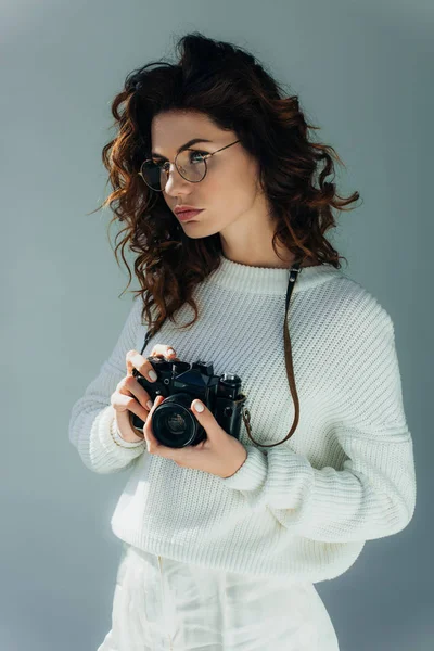 Belle jeune femme aux cheveux roux tenant appareil photo numérique sur gris — Photo de stock