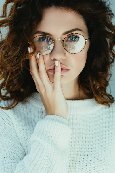 Séduisante jeune femme aux cheveux roux touchant le visage et regardant la caméra sur gris — Photo de stock