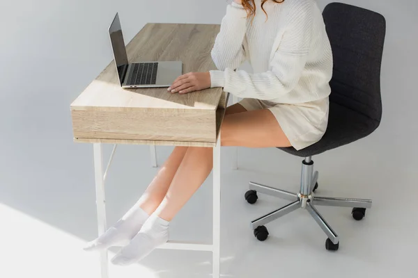 Vista recortada de la joven sentada cerca de la computadora portátil en gris - foto de stock