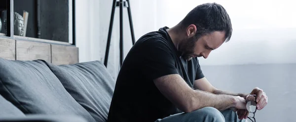 Panoramic shot of depressed with closed eyes sitting on grey sofa at home — Stock Photo