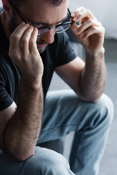 Расстроенный мужчина трогает очки, сидя дома на диване — стоковое фото