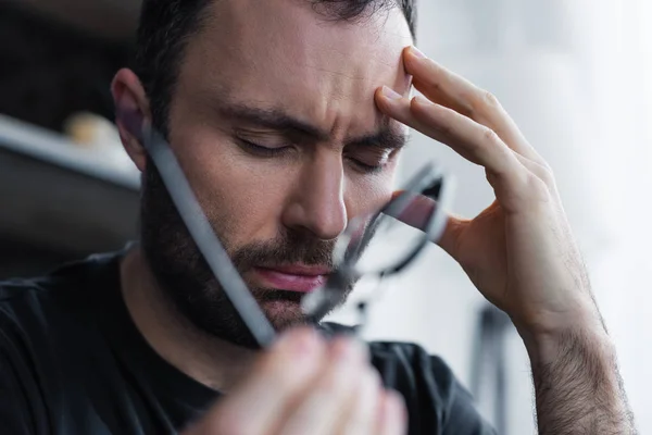 Enfoque selectivo del hombre frustrado con los ojos cerrados sosteniendo la mano cerca de la cabeza - foto de stock