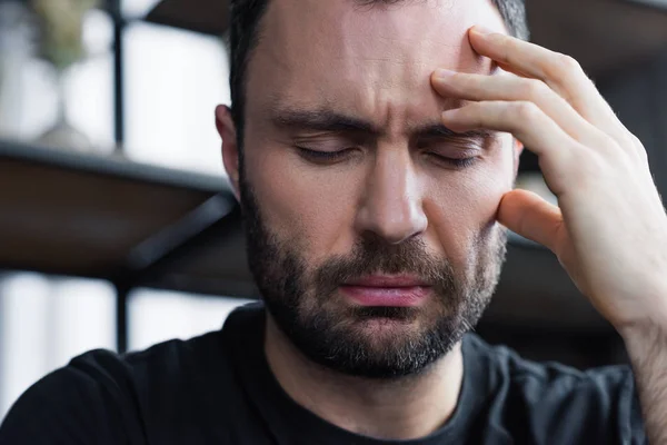 Trauriger unrasierter Mann, der mit geschlossenen Augen die Hand am Kopf hält — Stockfoto