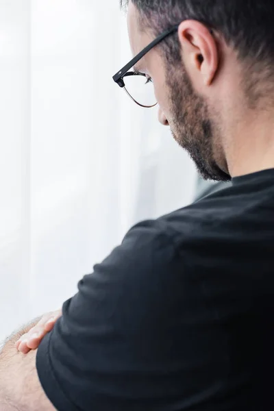 Unshaven depressed man in glasses standing by window at home — Stock Photo