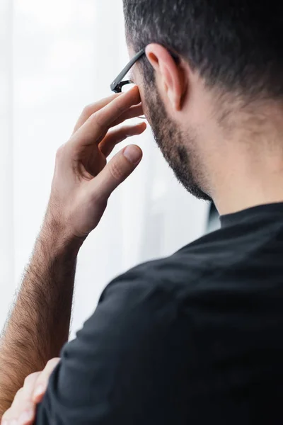 Rückansicht eines depressiven Mannes mit Brille, der die Hand vor dem Gesicht hält — Stockfoto