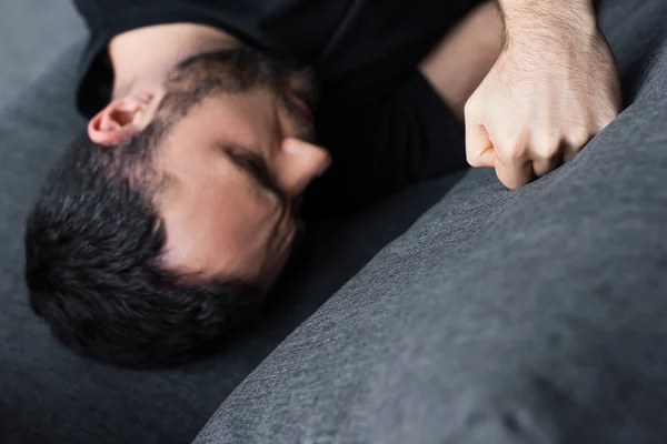 Overhead view of depressed man lying on sofa and kicking it with fist — Stock Photo