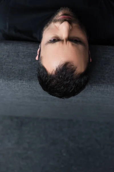 Vista aérea del hombre deprimido de pelo corto acostado en el sofá gris en casa - foto de stock