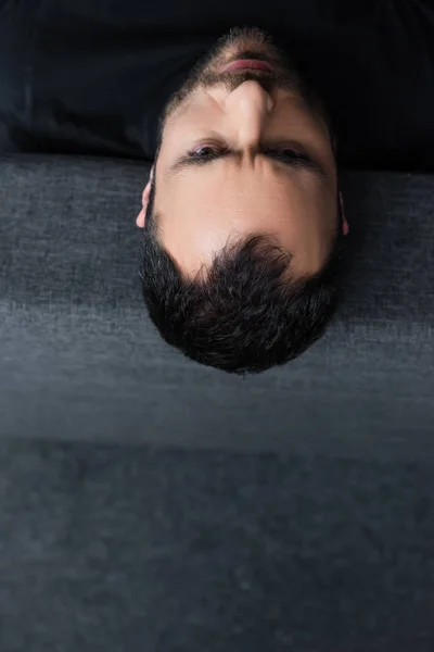 Overhead view of short haired depressed man lying on grey sofa at home — Stock Photo