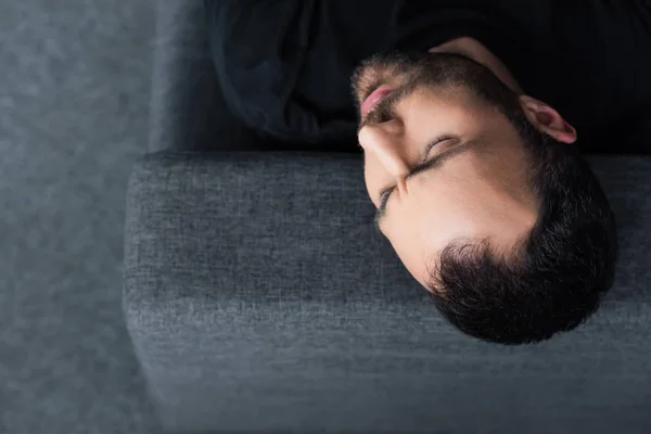 Vue aérienne de l'homme seul couché sur un canapé gris avec les yeux fermés — Photo de stock