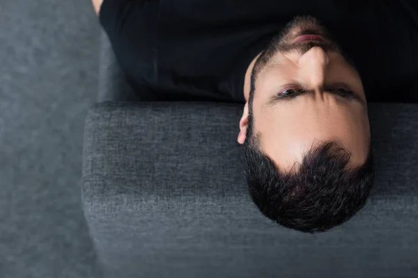 Vista aérea de un hombre guapo serio acostado en un sofá gris en casa - foto de stock