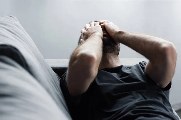 Hombre deprimido acostado en el sofá y sufriendo mientras se toma de la mano en la cara - foto de stock