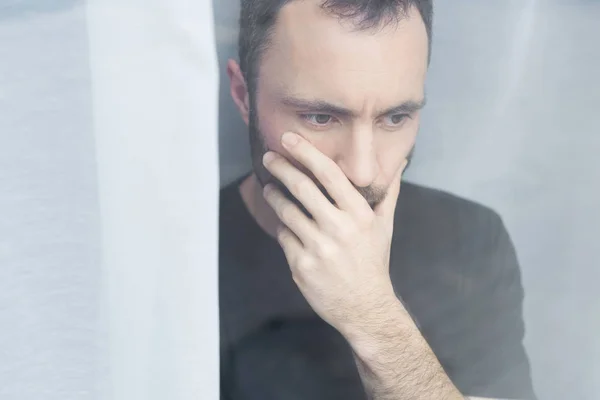 Bonito homem no preto t-shirt de pé por janela e segurando mão no boca — Fotografia de Stock