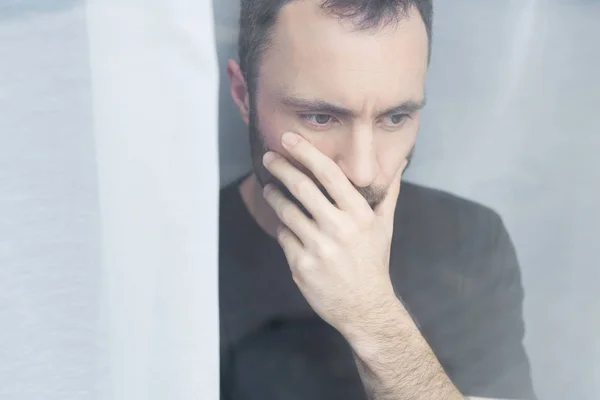 Handsome man in black t-shirt standing by window and holding hand on mouth — Stock Photo