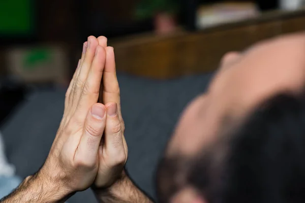 Partial view of lonely man holding praying hands while sitting at home — Stock Photo