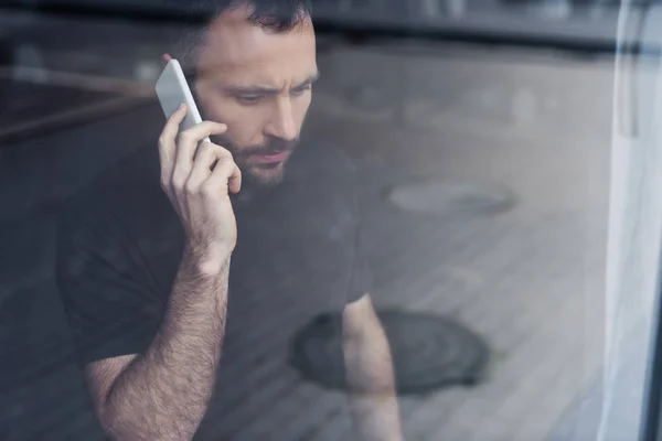 Seriöser Mann steht mit Smartphone am Fenster und schaut weg — Stockfoto