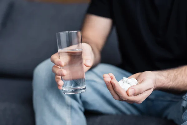 Partial view of man holding glass of water and handful of drugs — Stock Photo