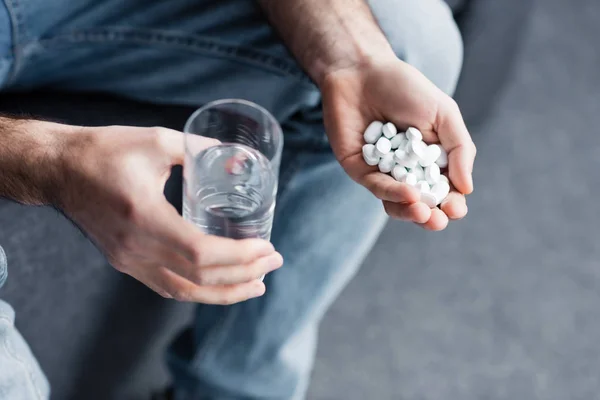Cropped view of sitting man holding handful of pills and glass of water — Stock Photo
