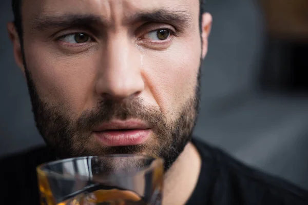Portrait of bearded crying man looking away while holding glass of whiskey — Stock Photo