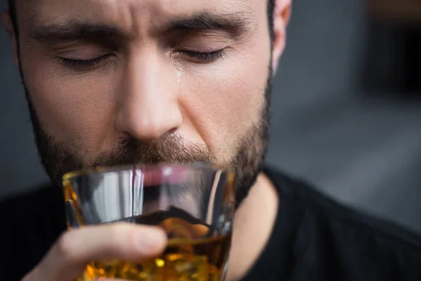 Messa a fuoco selettiva dell'uomo barbuto depresso che tiene un bicchiere di whisky ad occhi chiusi — Foto stock