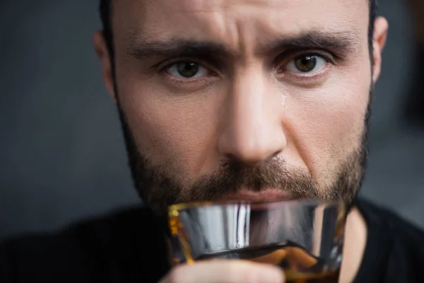 Избирательный фокус депрессивного мужчины, держащего стакан виски и смотрящего в камеру — стоковое фото