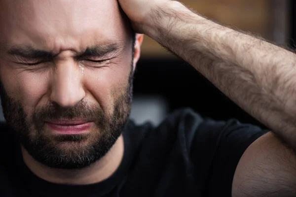 Hombre barbudo deprimido llorando con los ojos cerrados y sosteniendo la mano en la cabeza - foto de stock