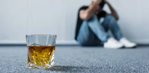 Вибірковий фокус депресивного чоловіка, що сидить на підлозі біля склянки віскі — стокове фото