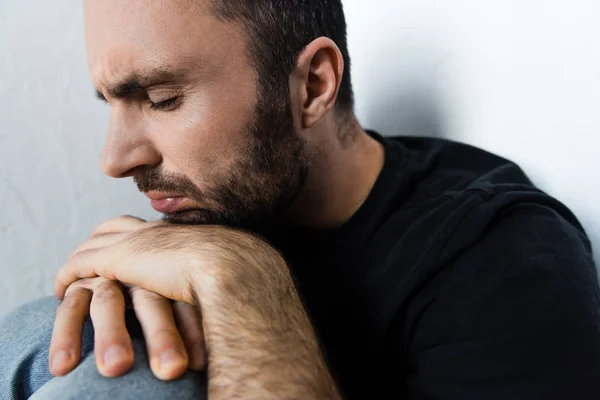 Adulto deprimido hombre que sufre sentado por la pared blanca con los ojos cerrados - foto de stock