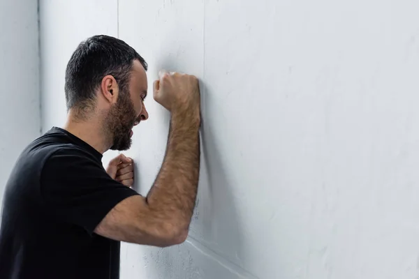 Adulto depresso uomo urlando mentre in piedi da parete bianca a casa — Foto stock