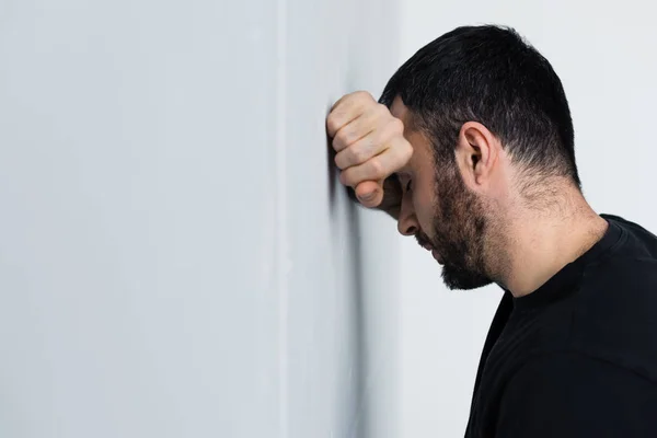 Deprimido hombre sin afeitar de pie cerca de la pared blanca con los ojos cerrados - foto de stock